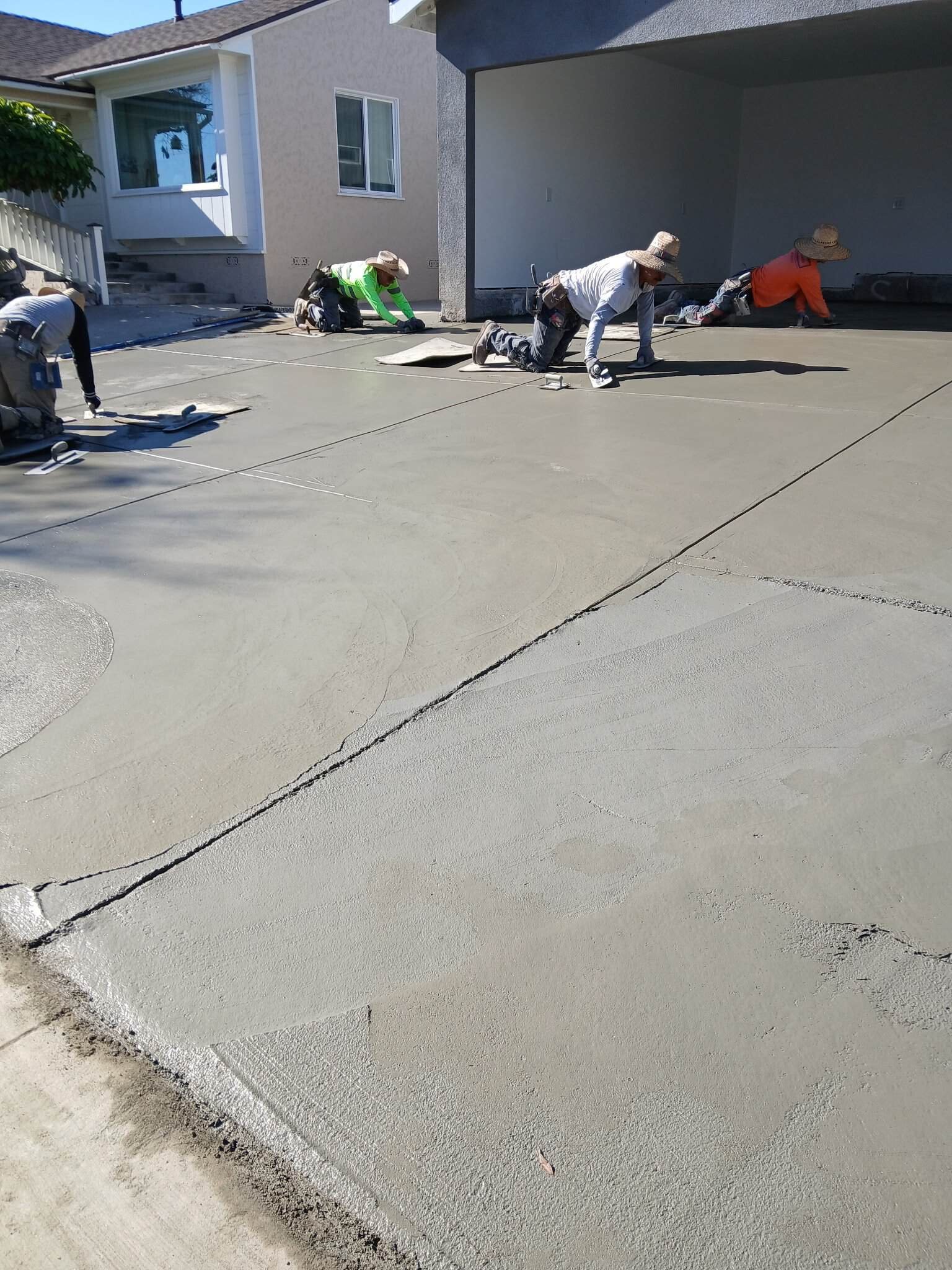 Skilled workers pouring and finishing concrete driveway in residential area.
