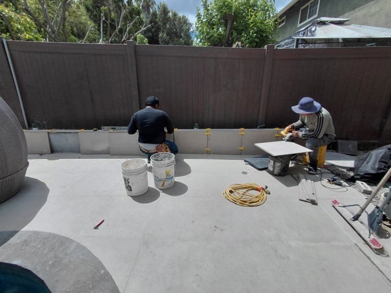 Two workers pouring and finishing concrete on a backyard patio.