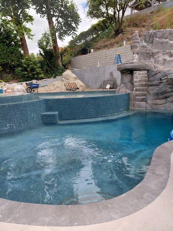 Custom concrete pool deck with waterfall feature and textured surfaces.